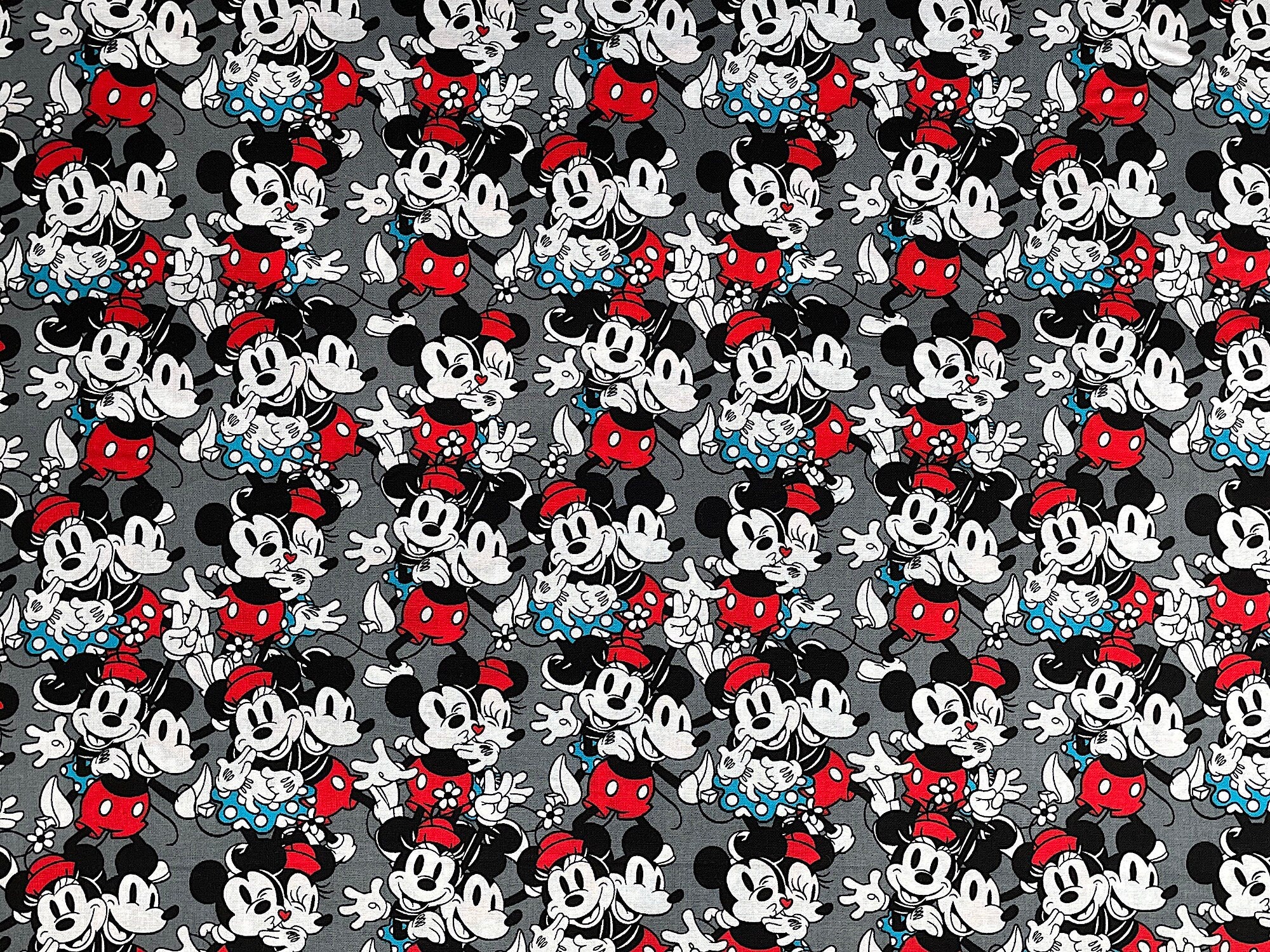This grey fabric is covered with Mickey and Minnie Mouse. This vintage fabric features Mickey and Minnie in love. Minnie is wearing a turquoise dress and red hat and Mickey has red shorts and a black shirt.