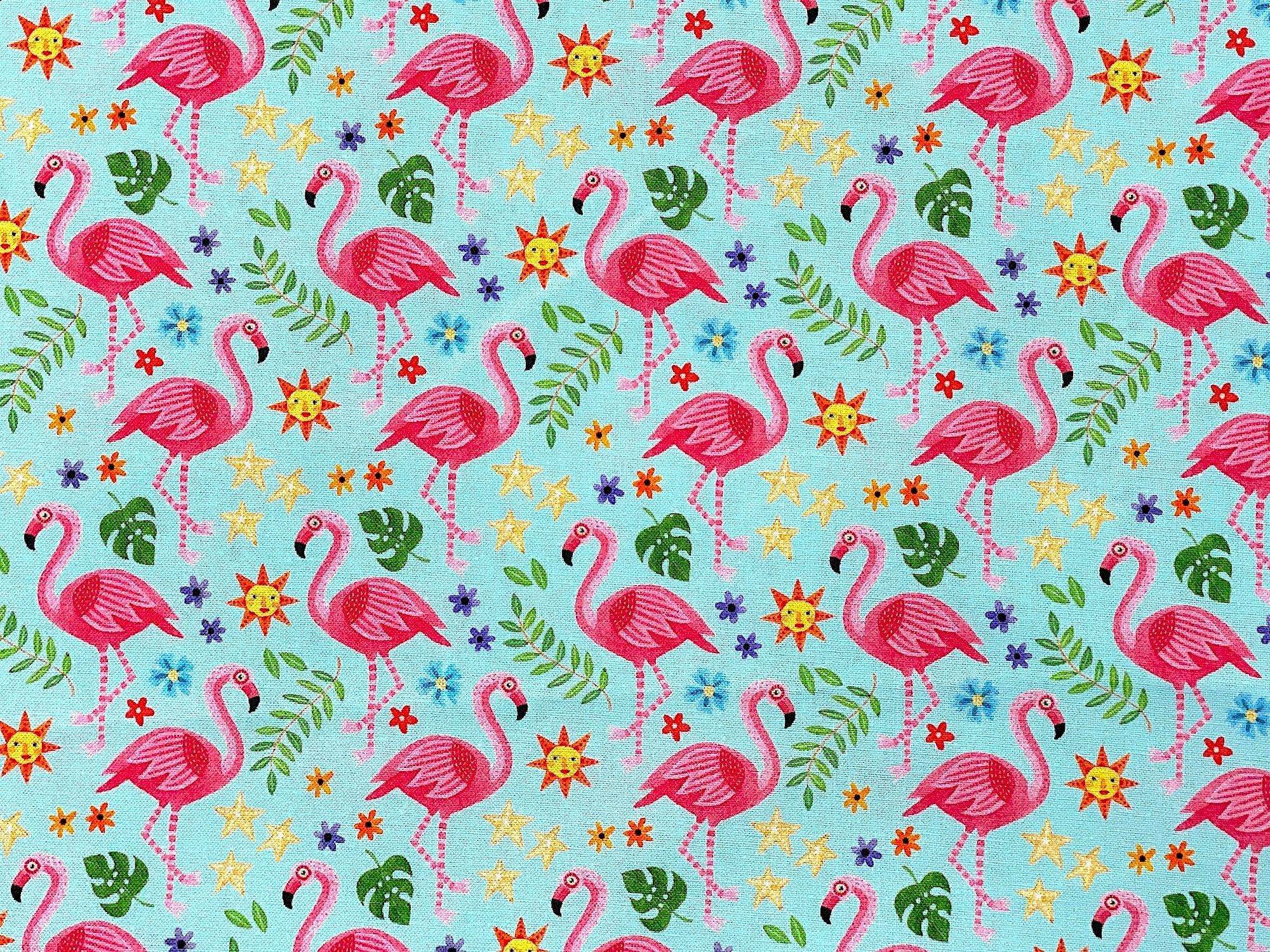 This fabric has an overall pattern of Flamingos, Suns, Stars, Flowers & Green Leaves. The background is a light turquoise blue.