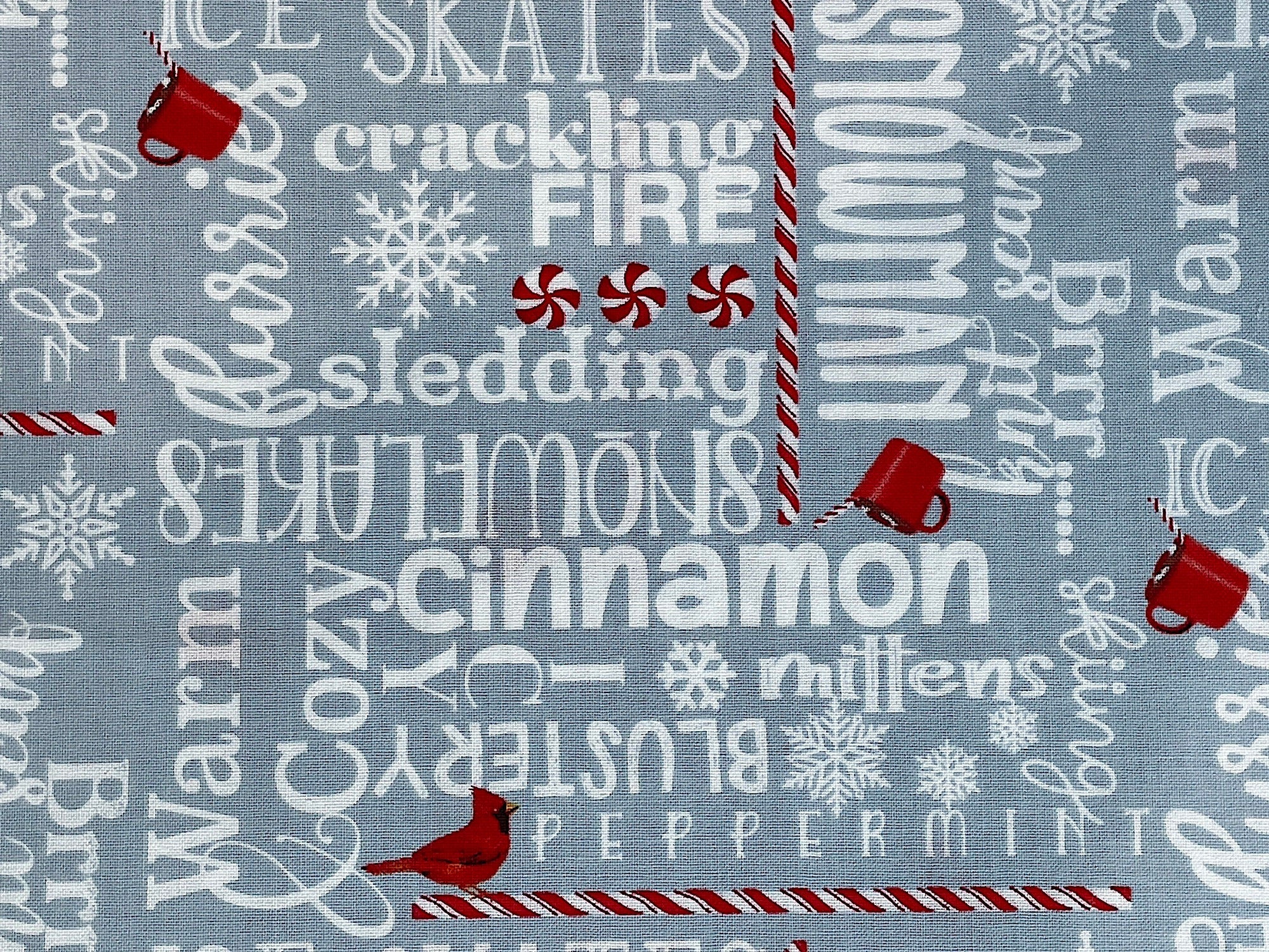 This gray cotton fabric is covered with winter words such as snowman, cinnamon, mittens, peppermint, crackling fire, ice skates and more. You will also find small red birds and red cups of cocoa throughout the fabric along with peppermint sticks.