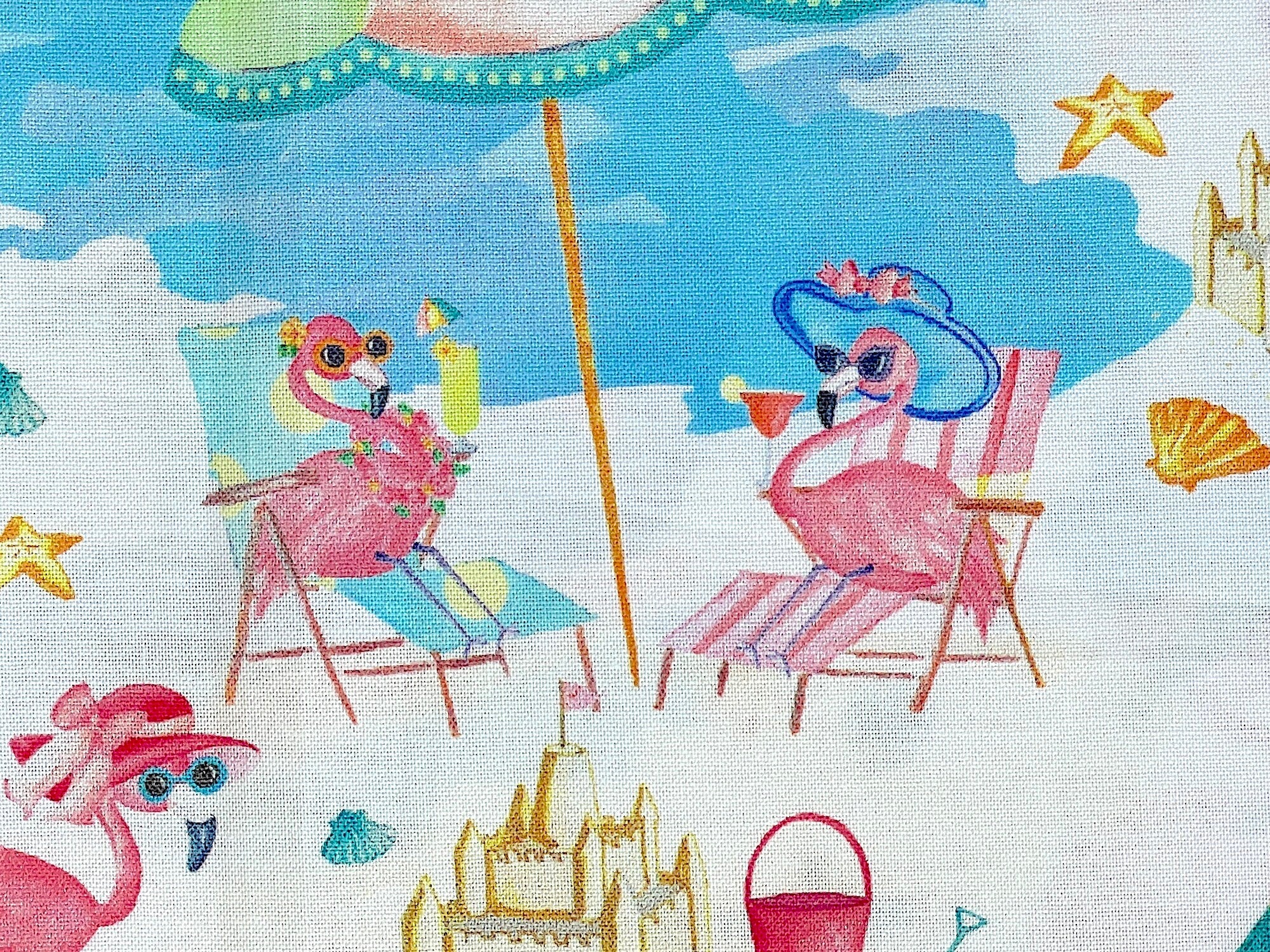Close up of flamingoes on the beach sitting in beach chairs enjoying a beverage.