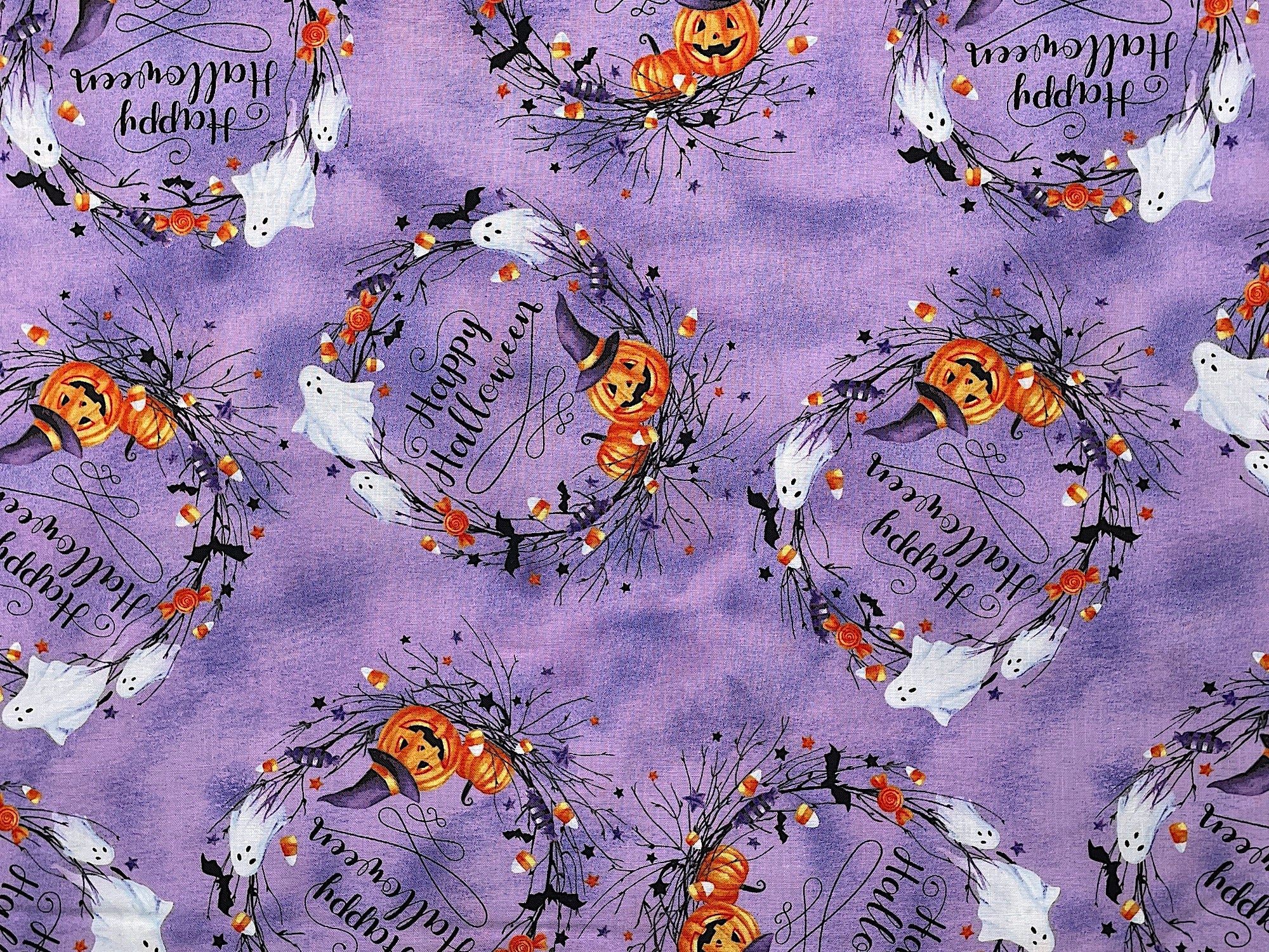Cotton fabric covered with Halloween Wreaths. The wreaths have ghosts, pumpkins, bats, jack-o-lanterns, candy corn and more. The background of this cotton fabric has shades of lavender and purple.