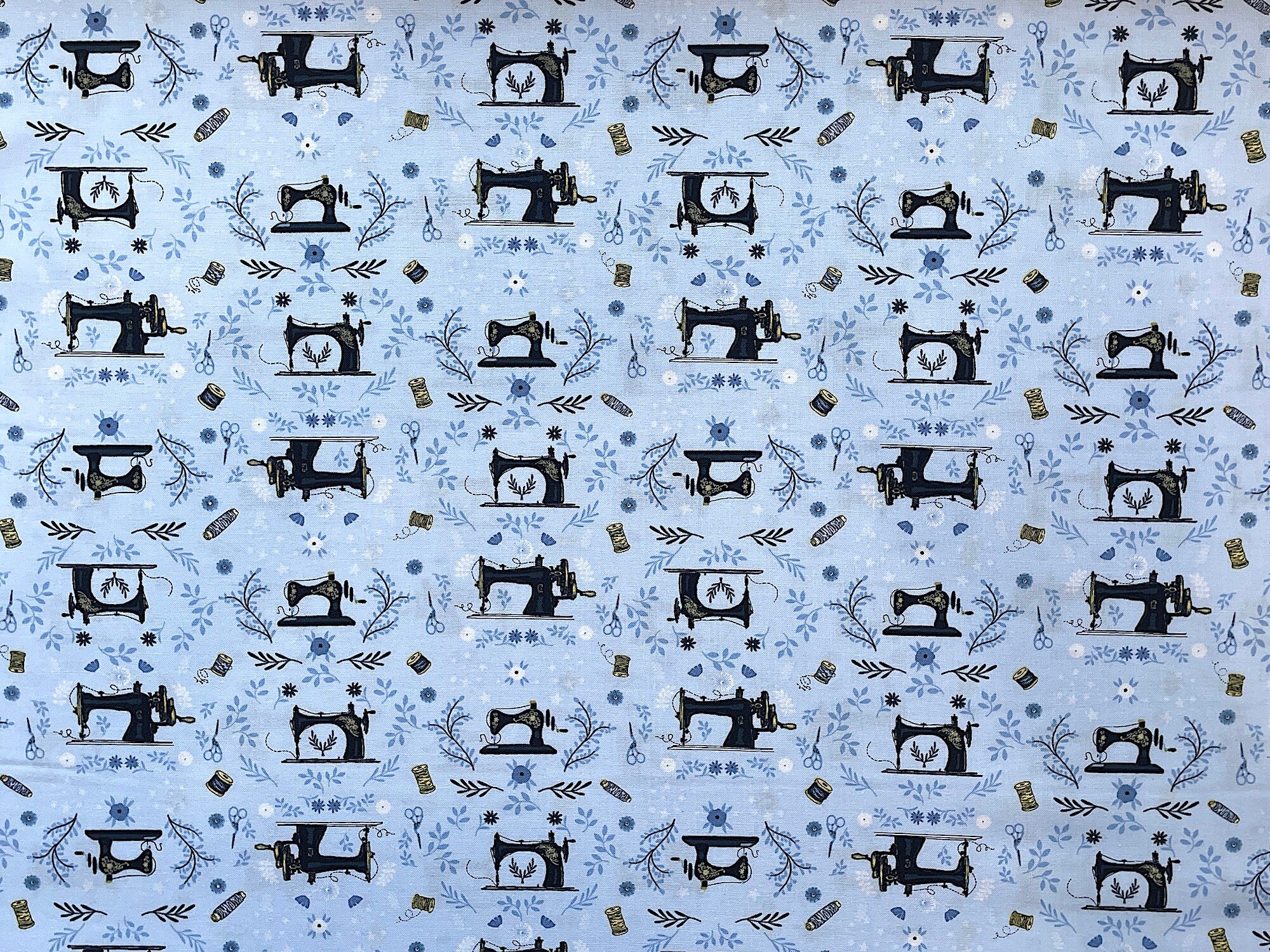 Blue cotton fabric covered with black sewing machines and spools of thread.