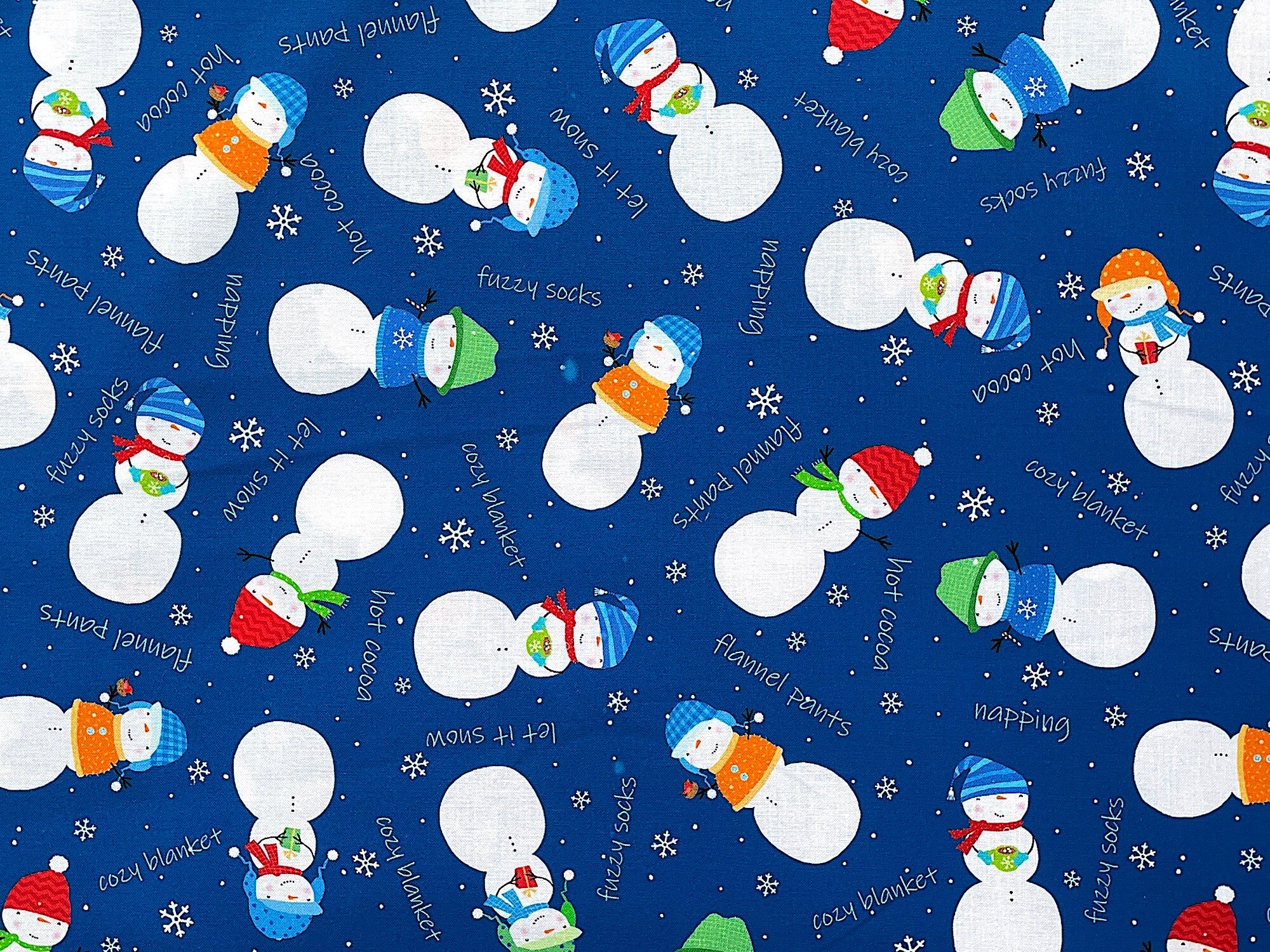 This blue fabric is covered with snowmen. The snowmen are wearing winter hats, some have scarves on or are holding a present or hot cocoa. Winter sayings such as flannel pants, fuzzy socks, napping, cozy blanket, hot cocoa are printed throughout the fabric. This fabric is part of the Winter Park collection by P&B Textiles.