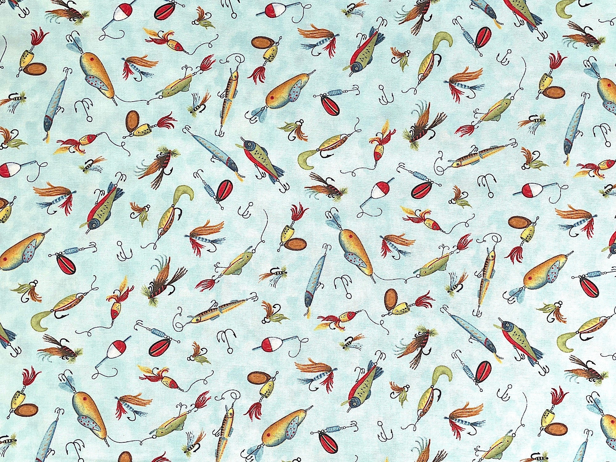 This blue fabric is covered with green, yellow, blue, black, white and red fishing lures. This fabric is part of the Down by the Lake collection by Wilmington Prints.