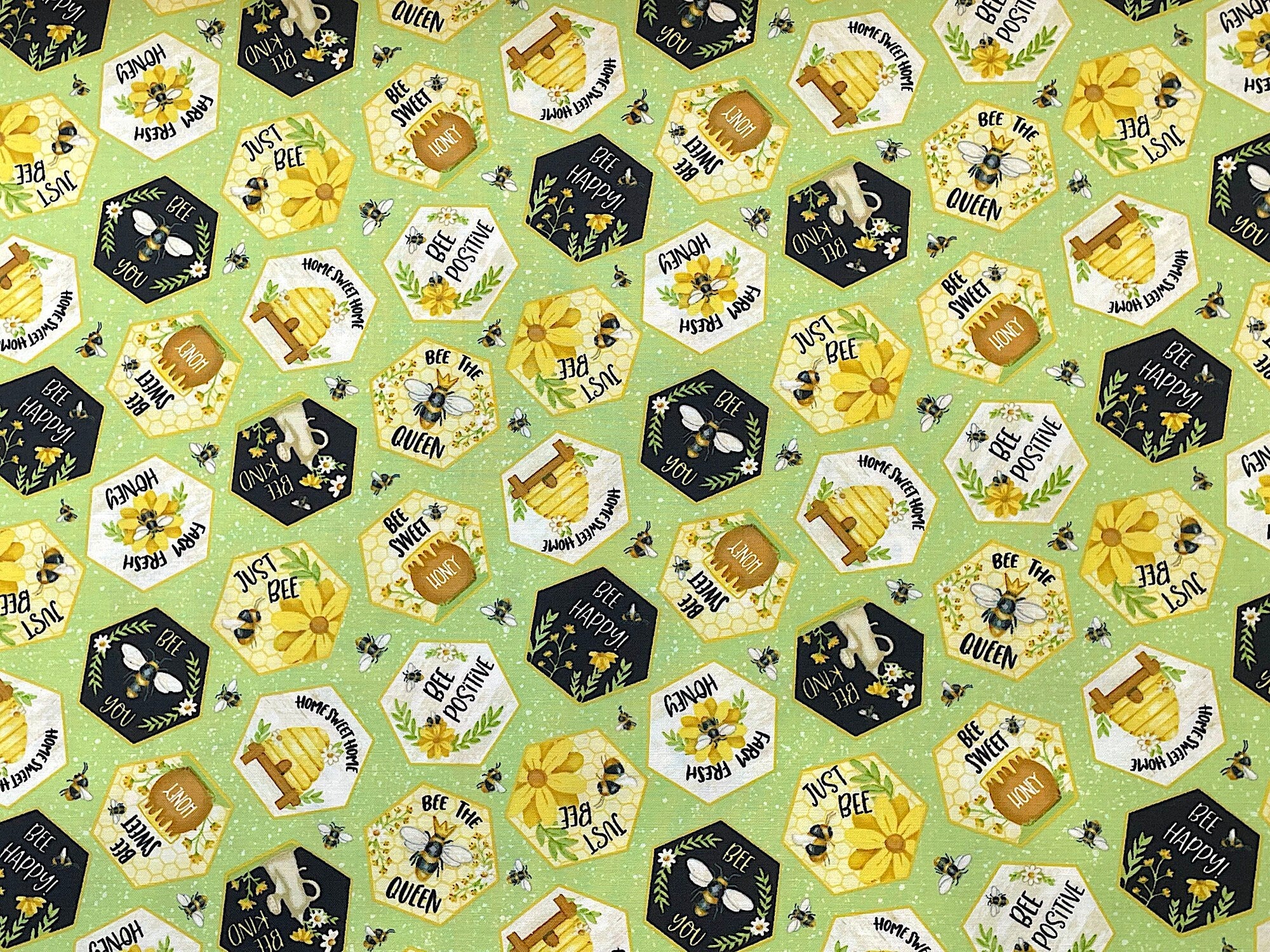Green cotton fabric covered with hexagons that have bees in them and positive sayings such as bee the queen, bee sweet and more.