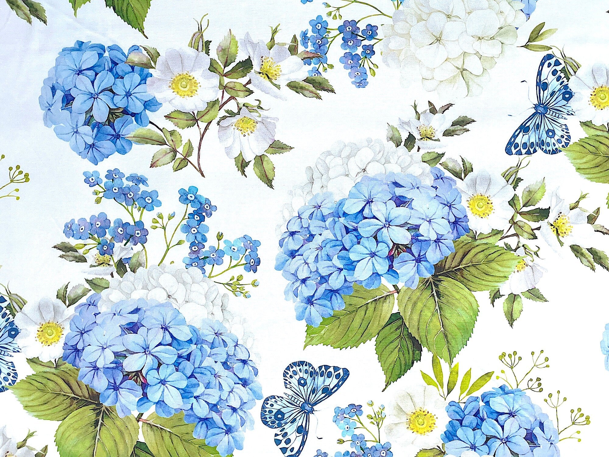 White cotton fabric covered with large blue and white hibiscus flowers and blue butterflies