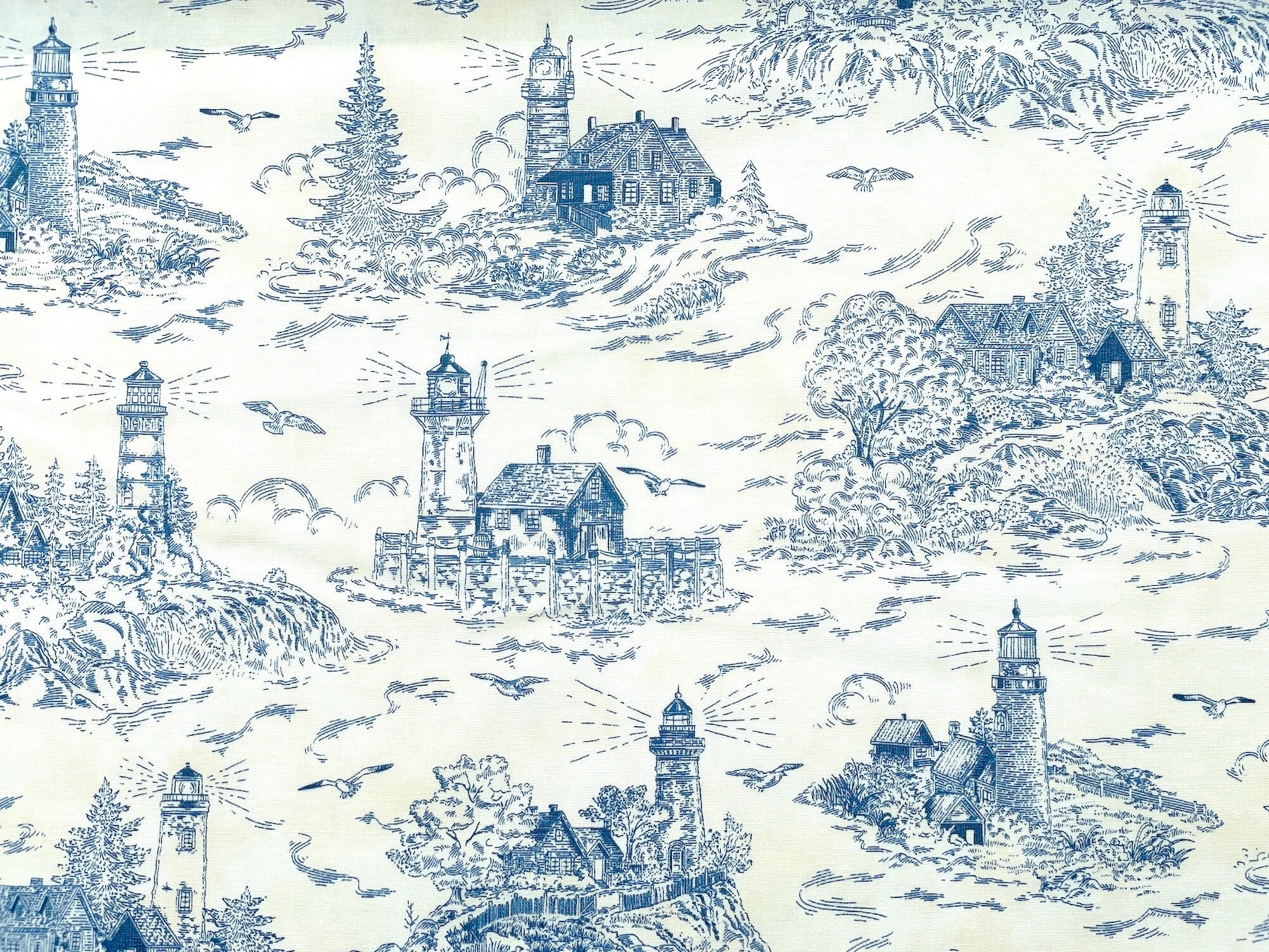 Cream colored fabric covered with bluework lighthouses, trees, water and more.