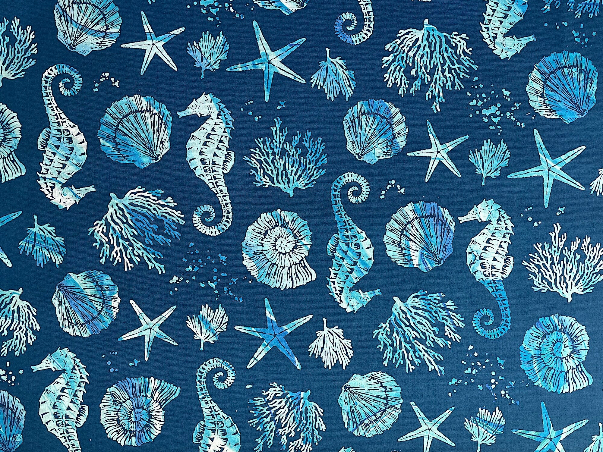 Blue cotton fabric covered with seahorses, starfish and coral.