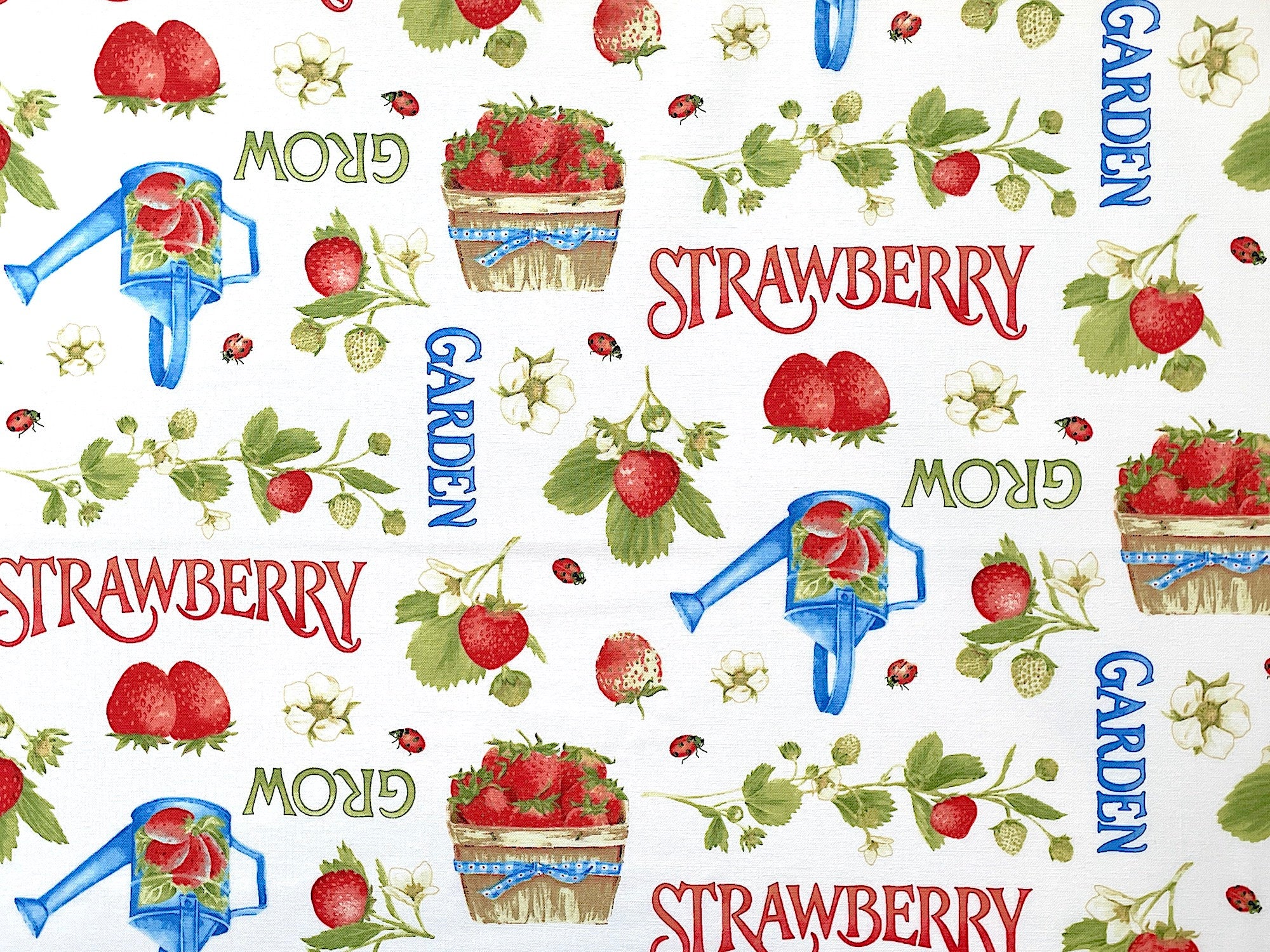 White cotton fabric covered with baskets of strawberries, watering cans and words such as garden grow and strawberry.