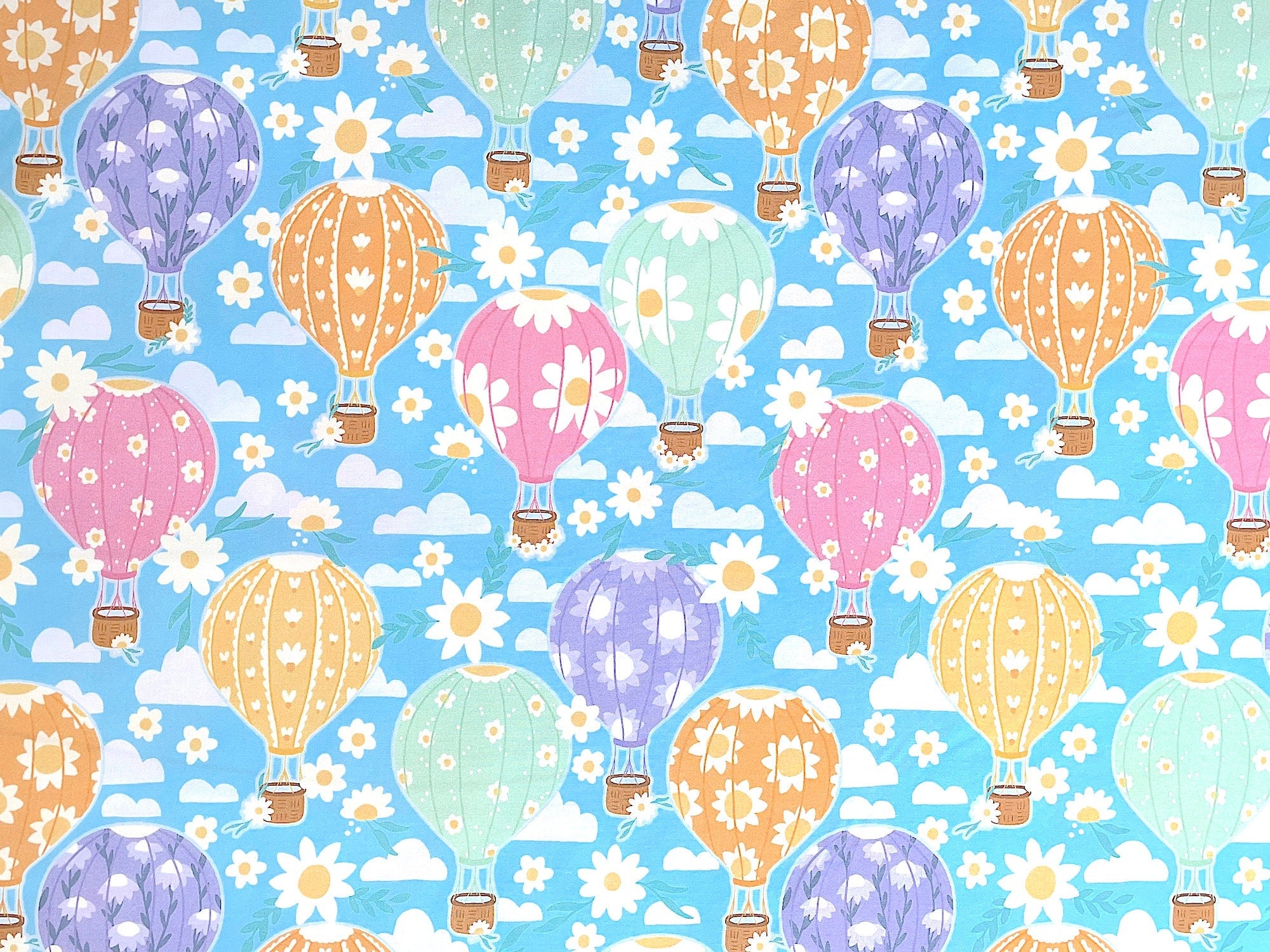 Blue cotton fabric covered with hot air balloons that are purple, pink, green.