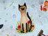 Close up of a Siamese cat sitting amongst the flowers with a butterfly on it's nose.