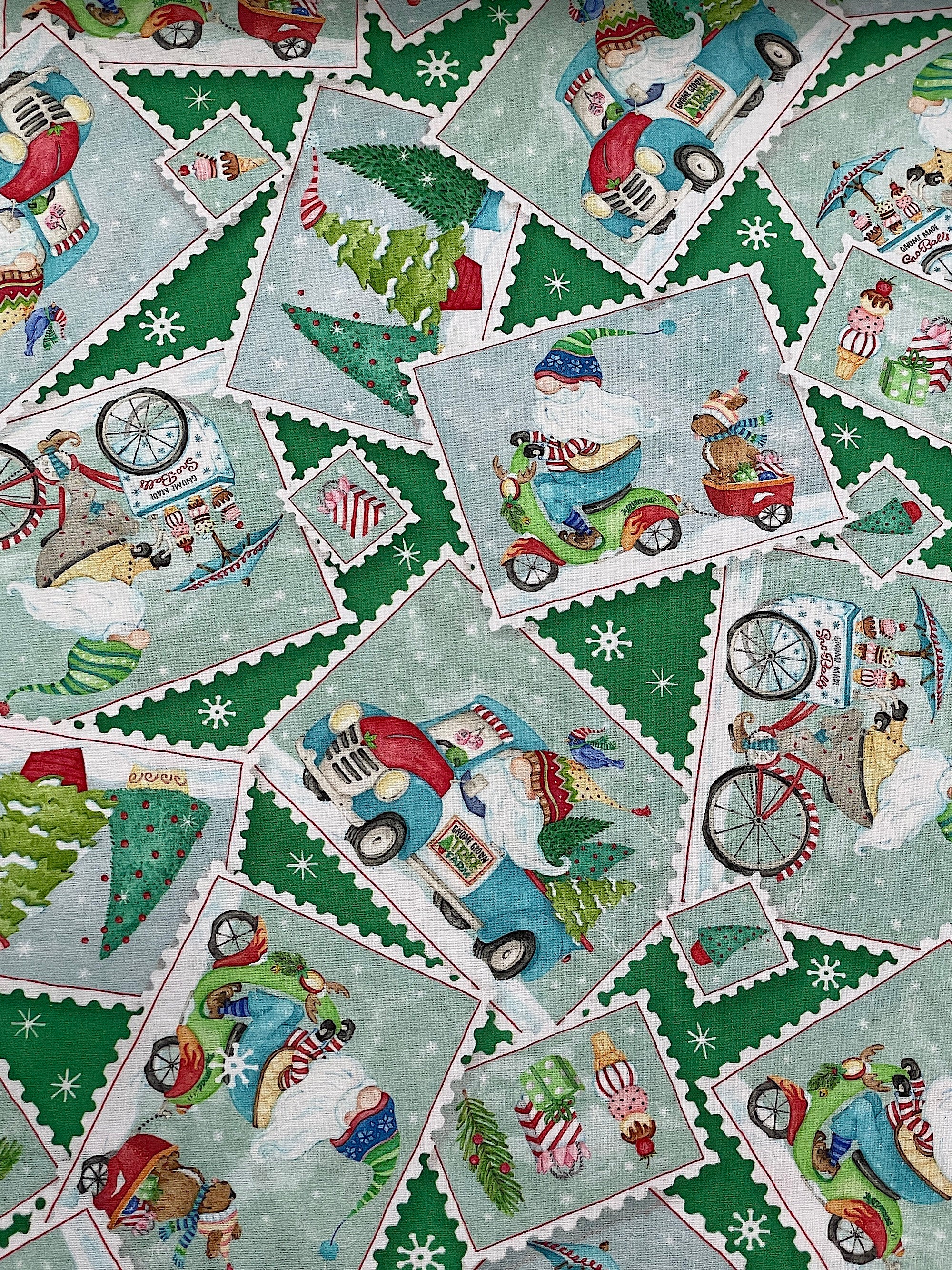 This fabric is part of the Wheeling Winter Wonderland collection by Robin Roderick. This green fabric is covered with postcards. the postcards have Santa gnomes, trees, trucks, bicycles, presents and more.
