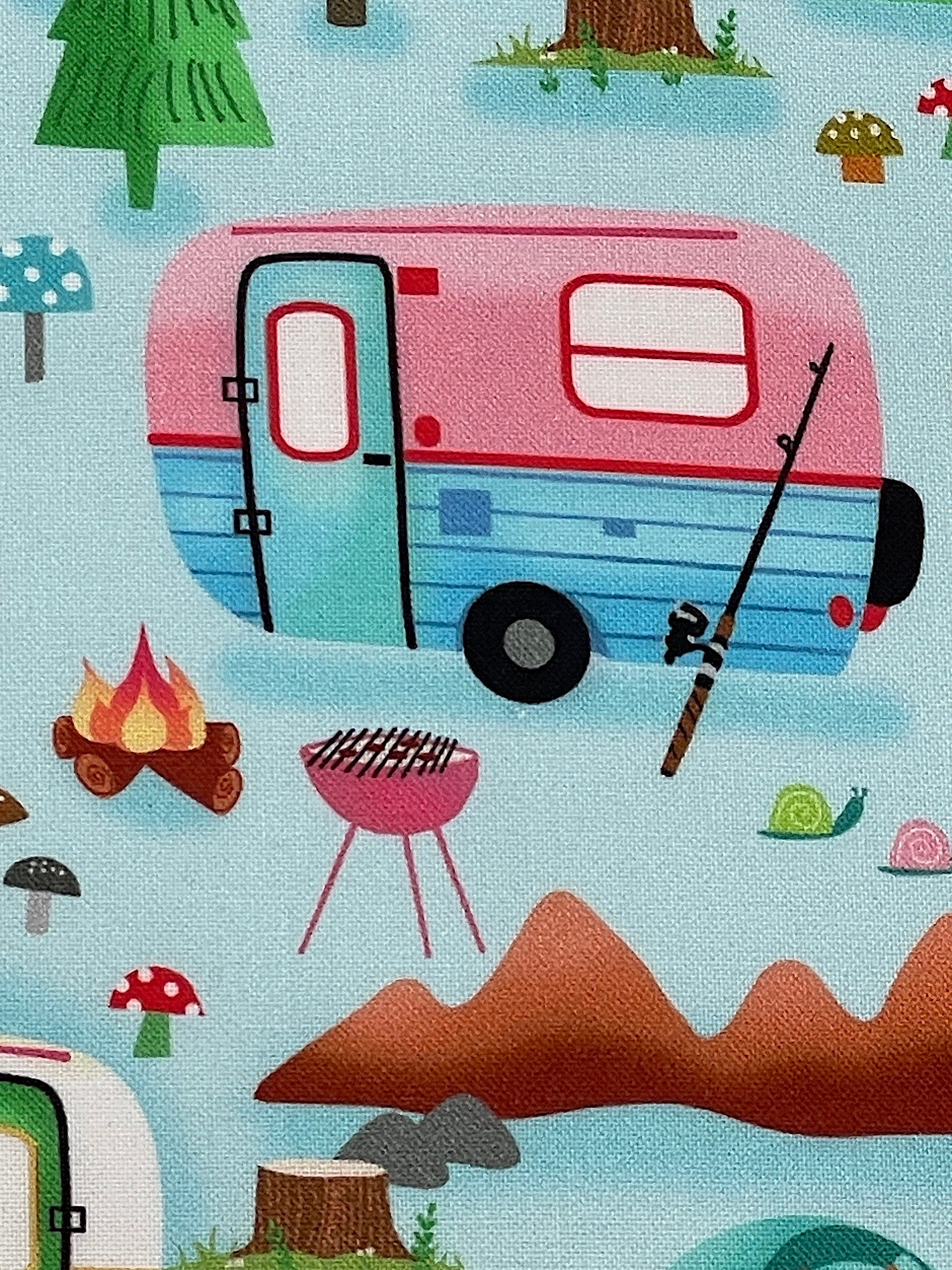 Close up of a pink, red and blue travel trailer with a fishing pole laying against it.