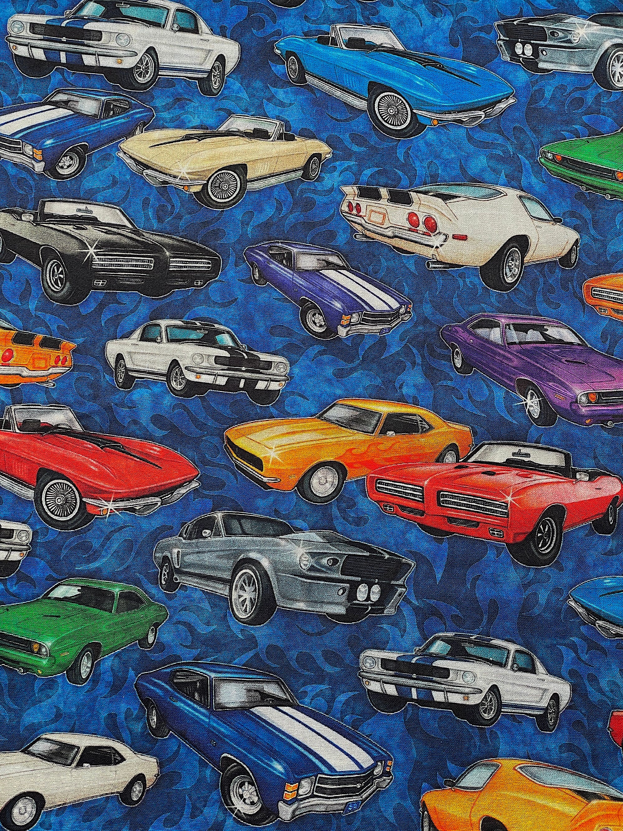 This blue cotton fabric is covered with old cars. The cars are white, green, blue, purple, blue, orange and black.