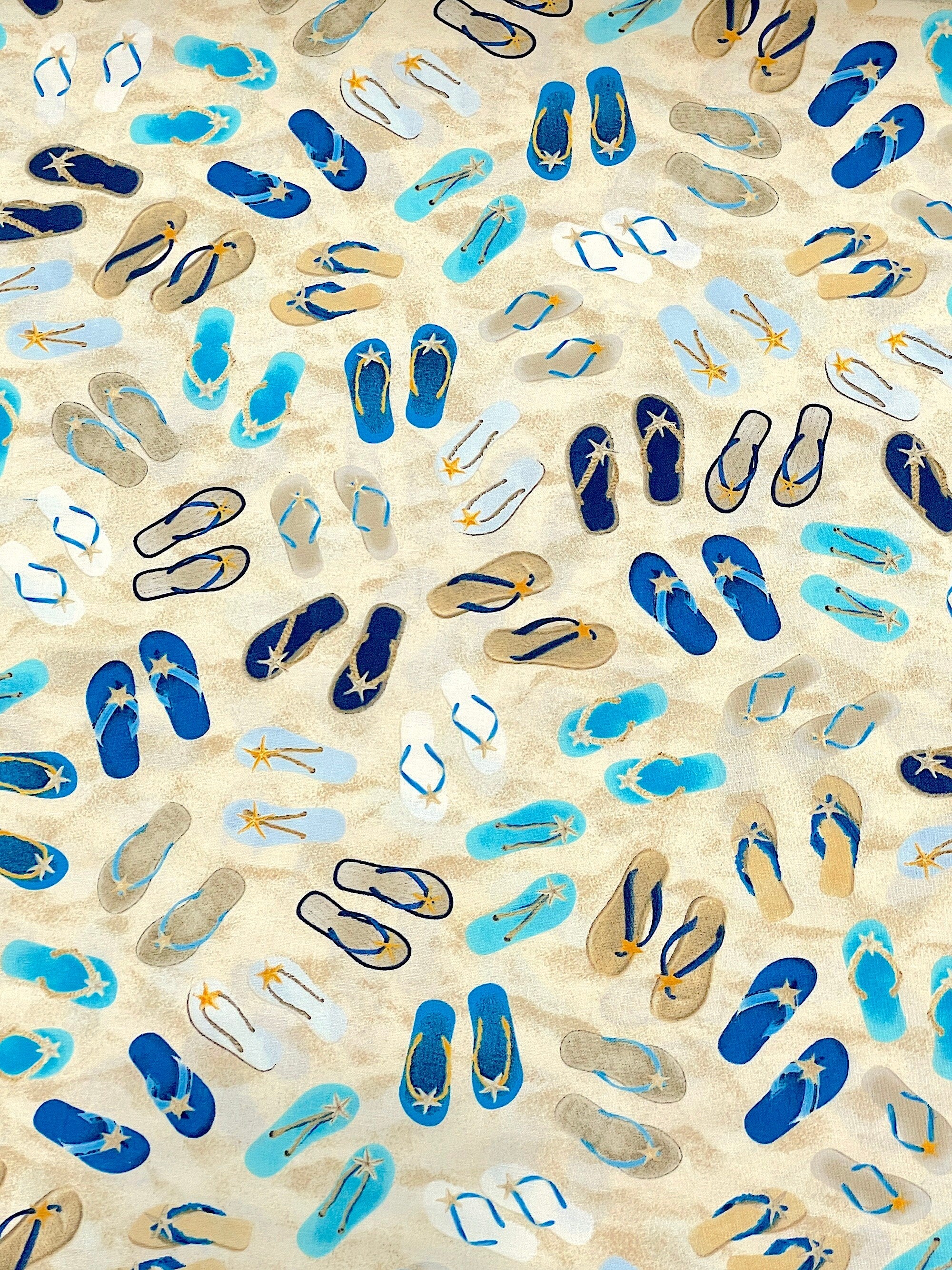 This fabric has a sand background and is covered with flips flops. The flip flops are blue, beige and white.